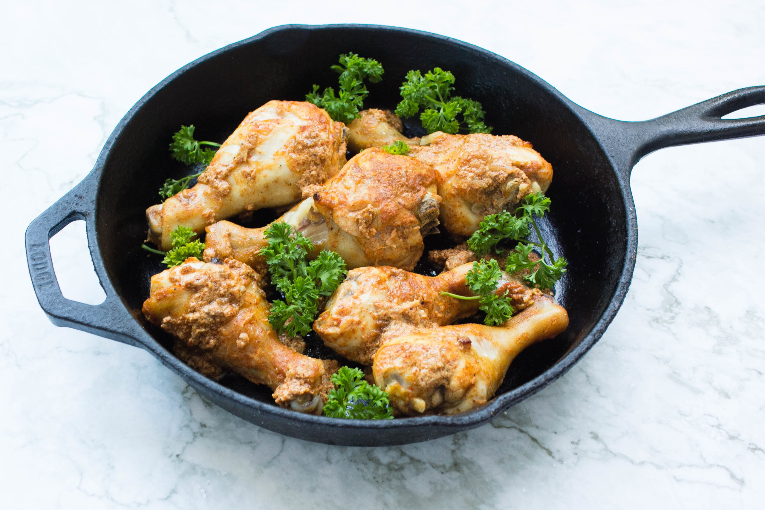 Pakistani chicken drumsticks in skillet with parsley garnish