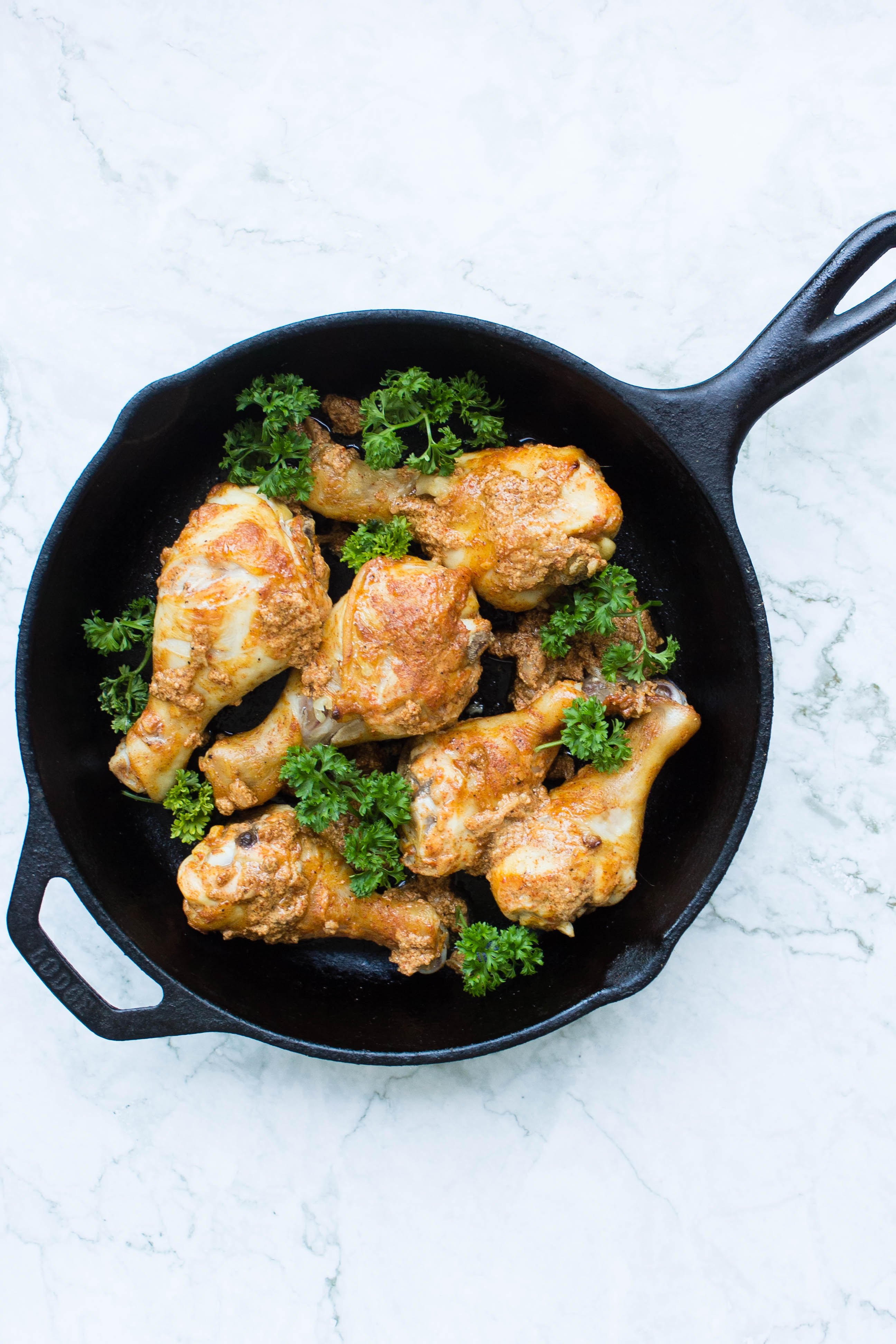 Pakistani chicken drumsticks in skillet with parsley garnish