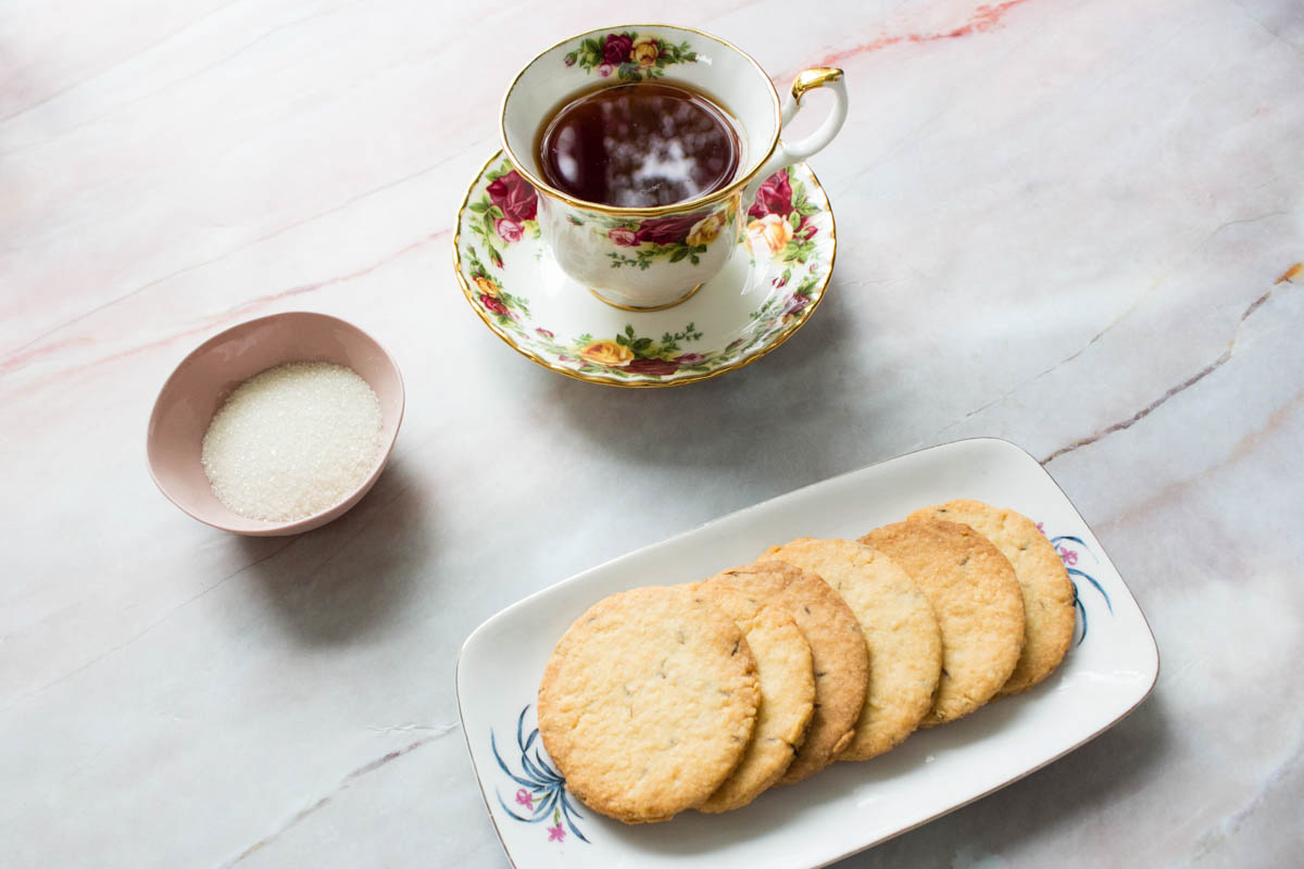 A cup of black tea, a bowl of sugar, and side of jeera biscuits 
