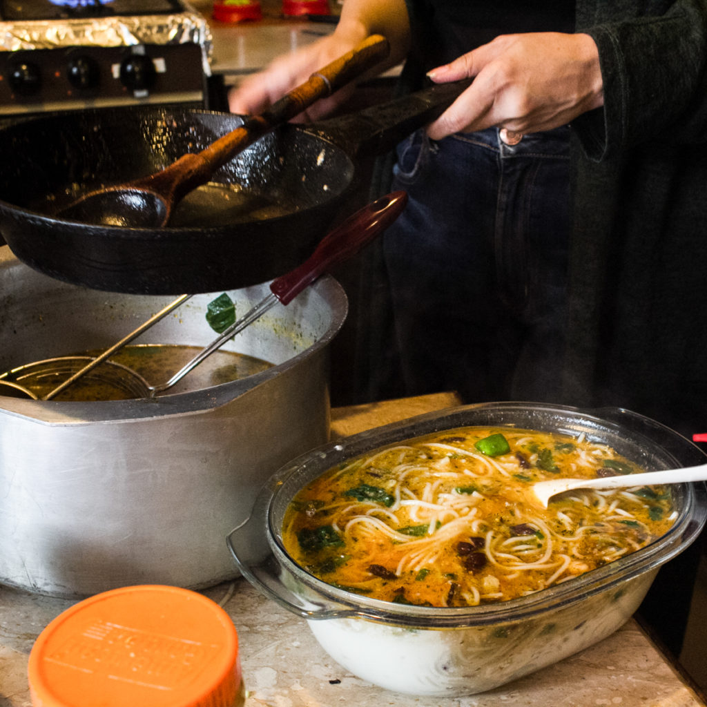 Woman transferring ash noodles from pot to serving dish