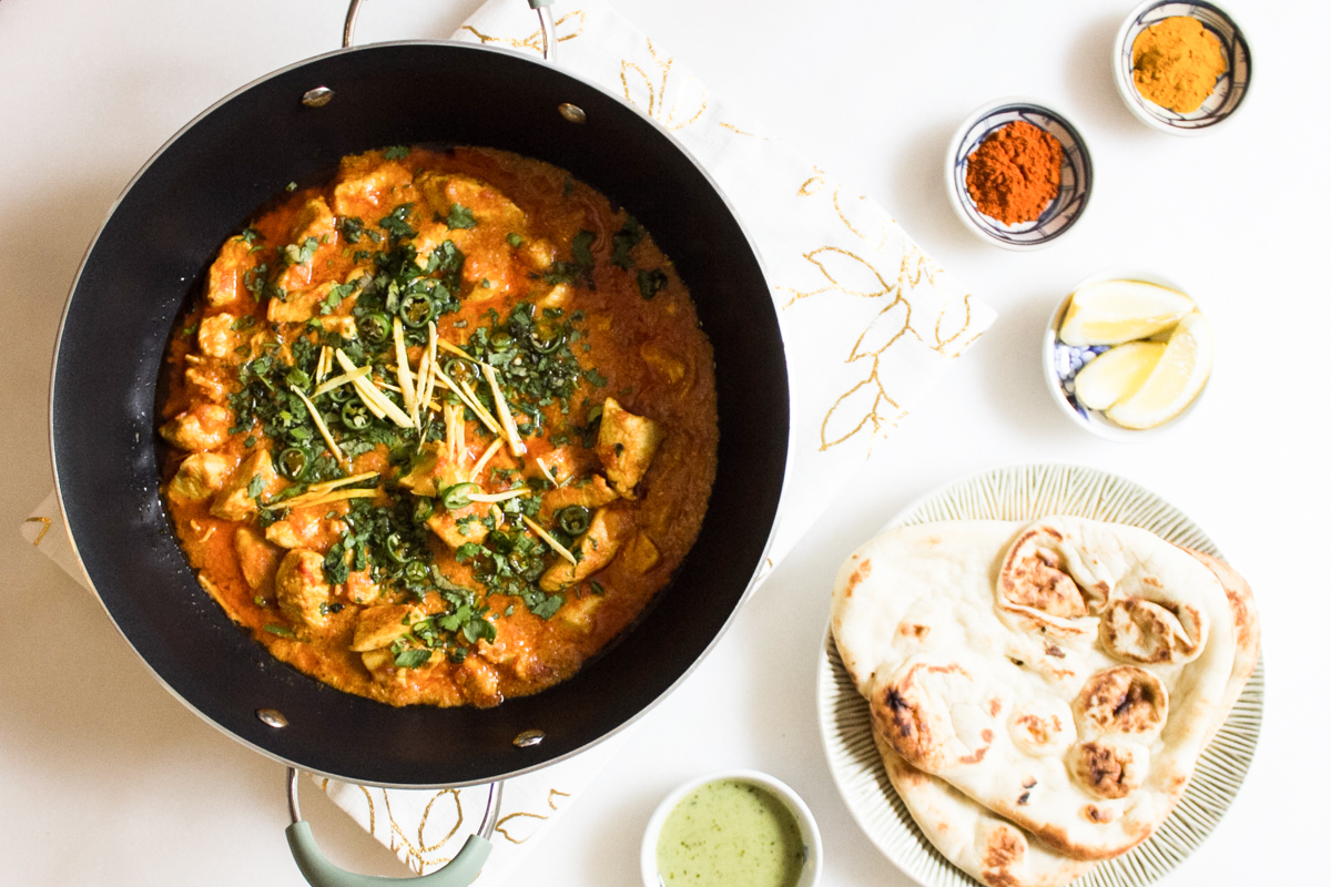 Pakistani ginger chicken in a wok served with naan, raita, lemon wedges.