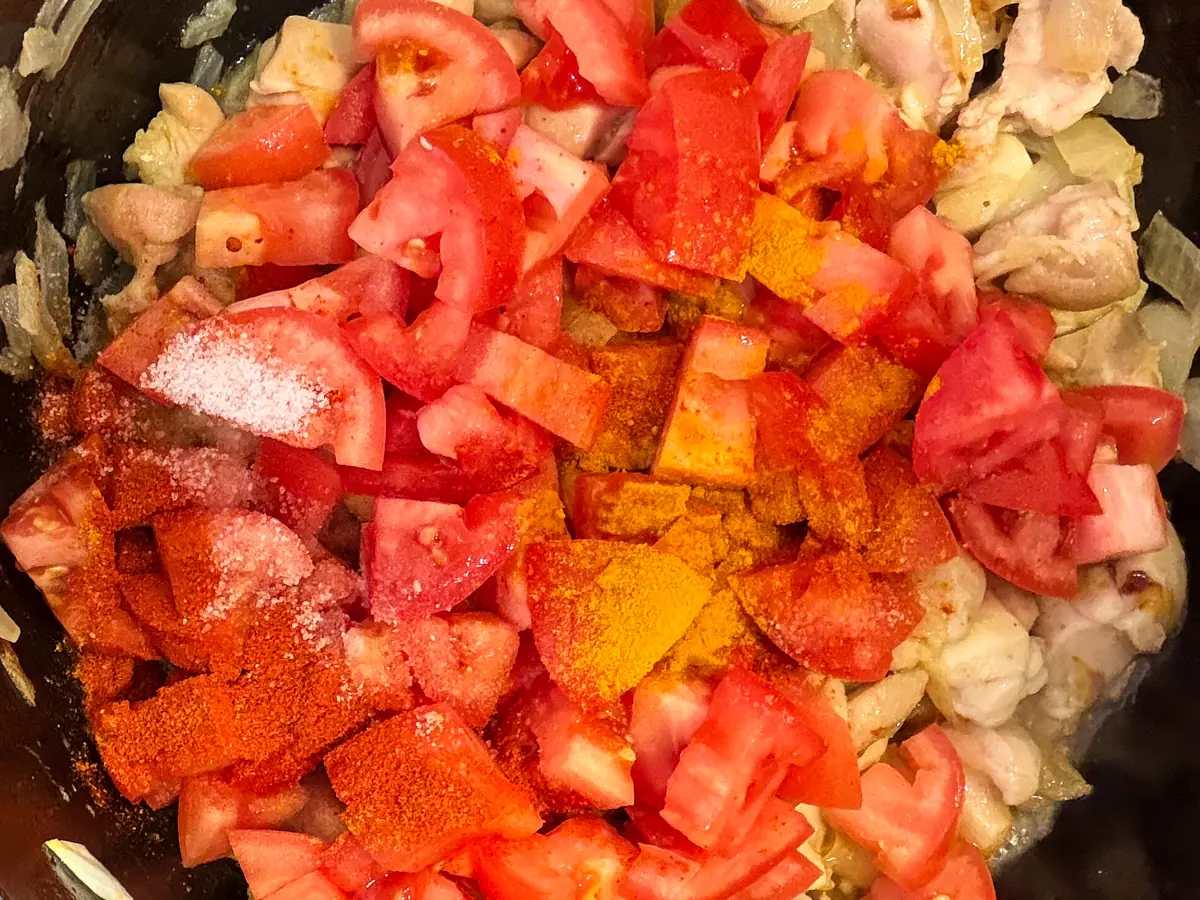 Chopped tomatoes and ground spices added to the chicken and onion mixture